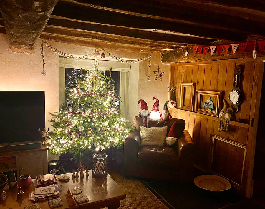 The cozy cottage living room decorated for Christmas 2021, with a Christmas tree by the patio doors.
