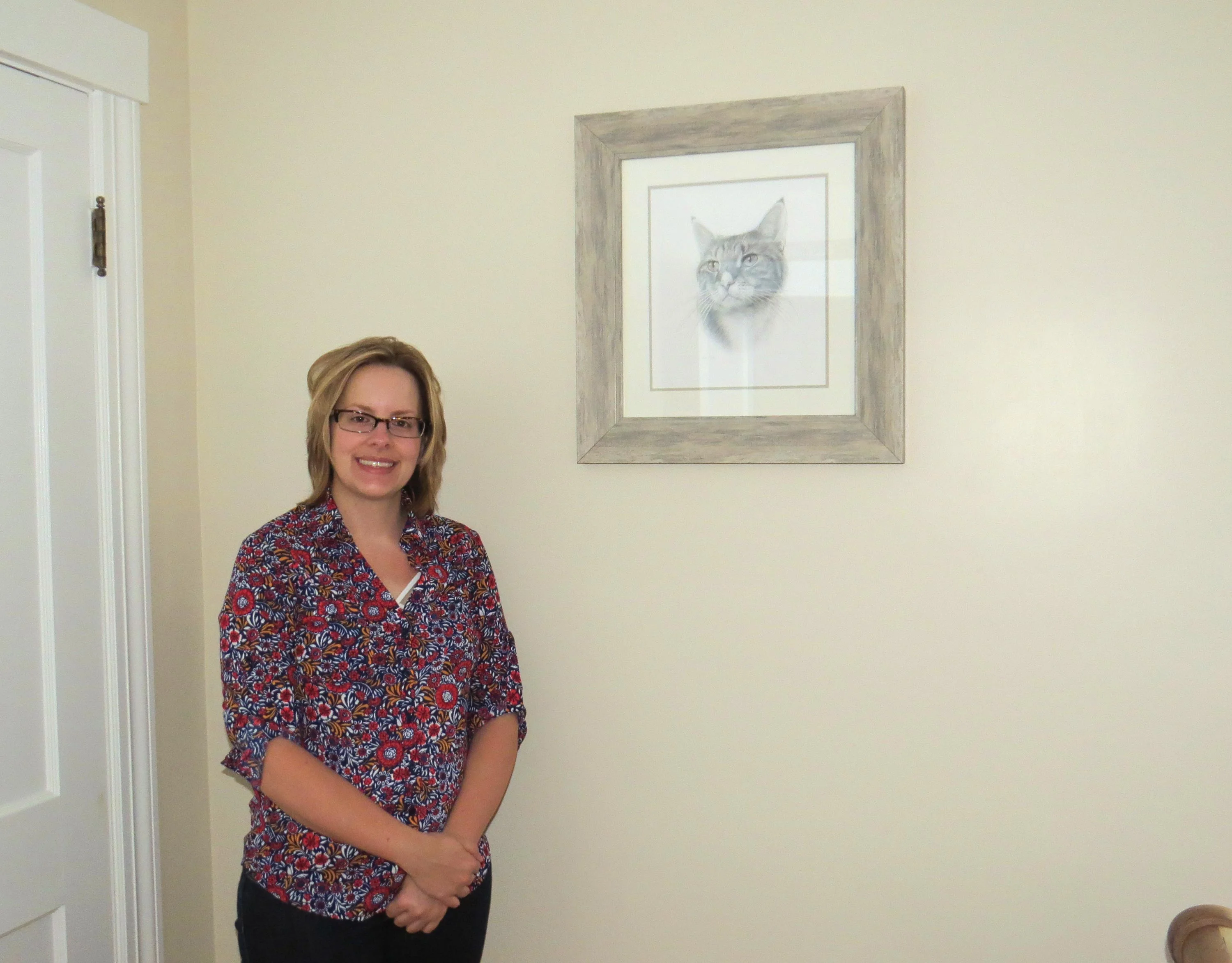 Client Kim holding the framed pencil portrait of her cat Tyson in her home.